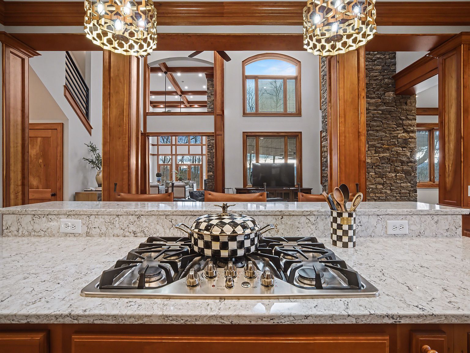 The kitchen with a gas range island, coffered ceiling, and wide view through to the great room