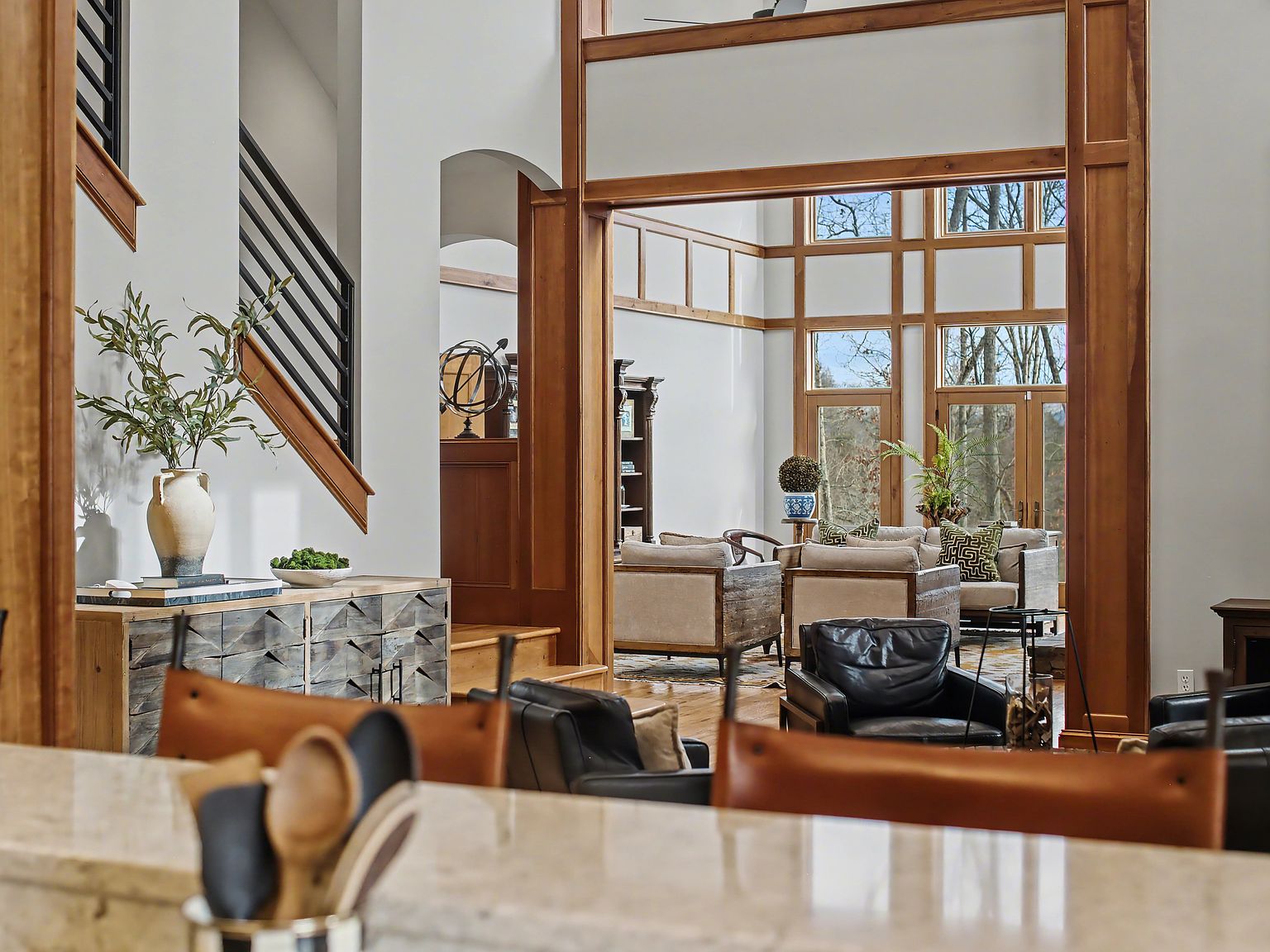 A view from the kitchen into the open living area with tall transom windows and a curved staircase