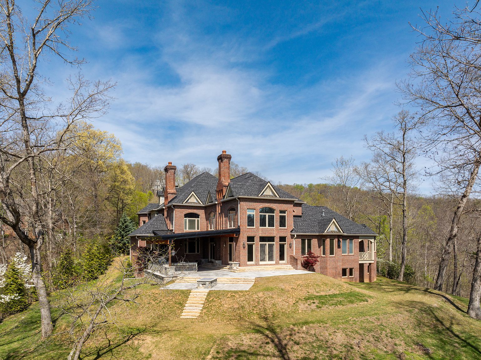 A custom brick estate with three chimneys and a stone terrace, set into a forested Tennessee ridge above a sloping lawn